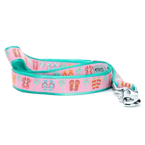 A colorful dog leash featuring a pattern of flip-flops, palm trees, and beach-themed motifs on a pink background.