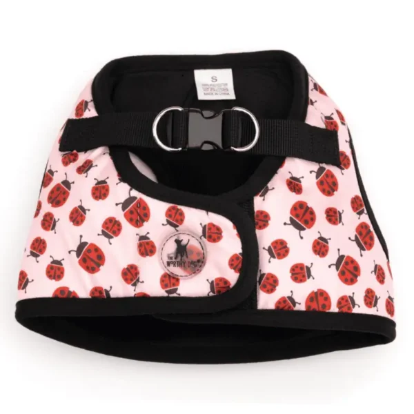 A pink dog harness with a ladybug pattern and a black trim, featuring a buckle and a D-ring for leash attachment.