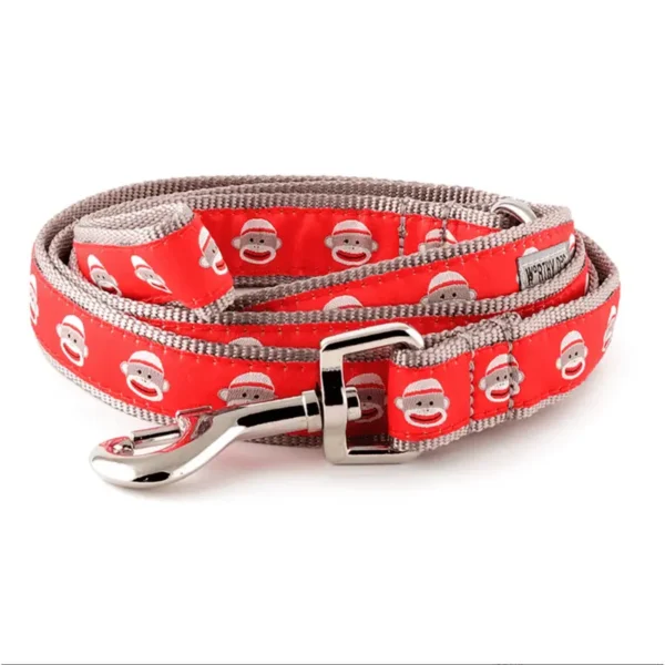 A red dog leash featuring a pattern of smiling sock monkey faces.