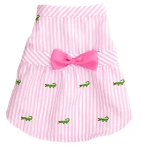 A pink striped dog dress with green alligator embroidery and a pink bow.