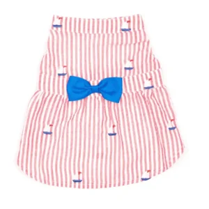 A red and white striped dog dress with a blue bow, featuring small blue sailboat designs.