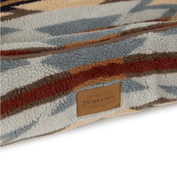 A close-up of a patterned pet bed in tan, gray, and brown with a fabric interior and a small label.