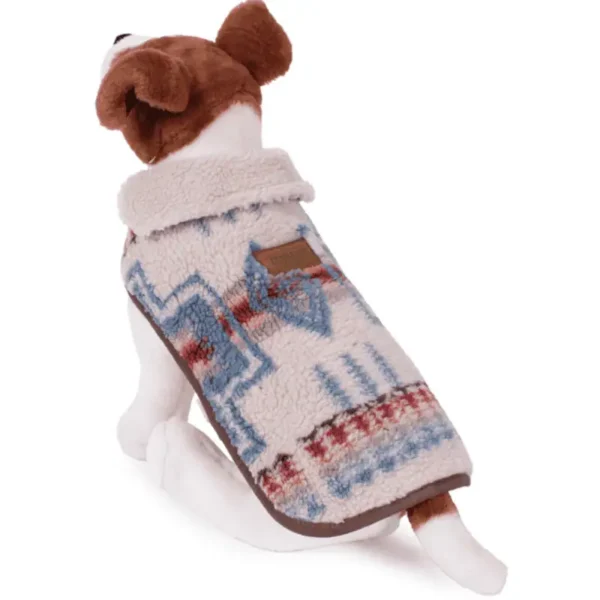 A small dog wearing a cozy fleece coat with a patterned design is sitting.