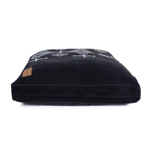 A black dog bed with decorative patterns on the top side and a label on one corner.