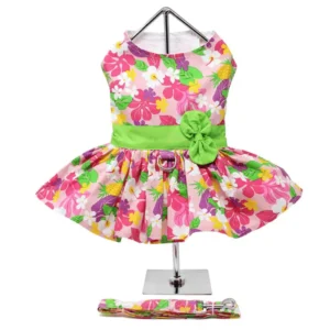 A colorful floral dog dress with a green waistband and matching flower embellishment, displayed on a stand, accompanied by a coordinating leash.