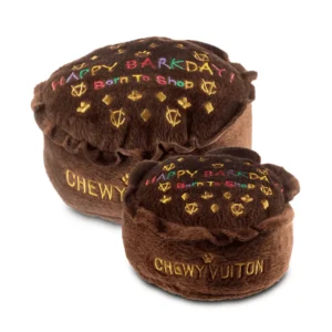 Plush brown Chewy Vuiton Barkday Cake dog toy topped with gold CV logos, gold diamond and clover designs, rainbow letters reading “Happy Barkday! Born To Shop,” and gold “Chewy Vuiton” text on the side. Soft squeaky toy for stylish pups.