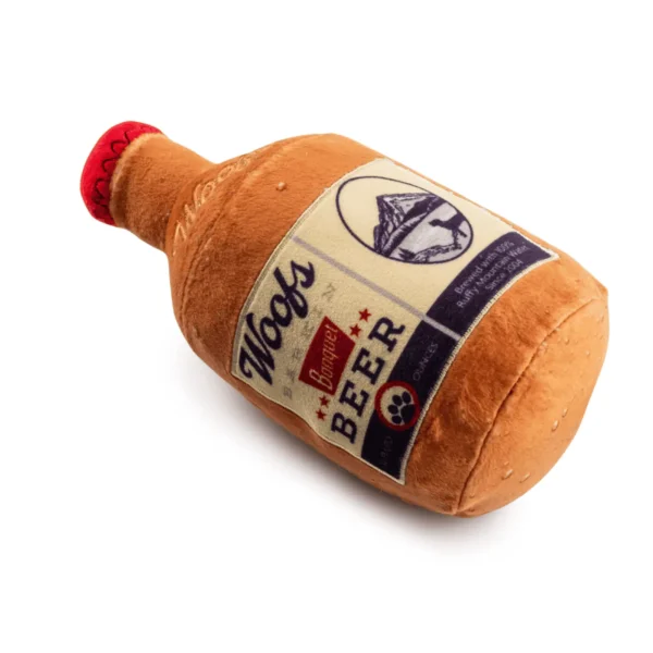 Slanted view of Plush brown beer bottle dog toy with tan Woofs Beer label and red cap